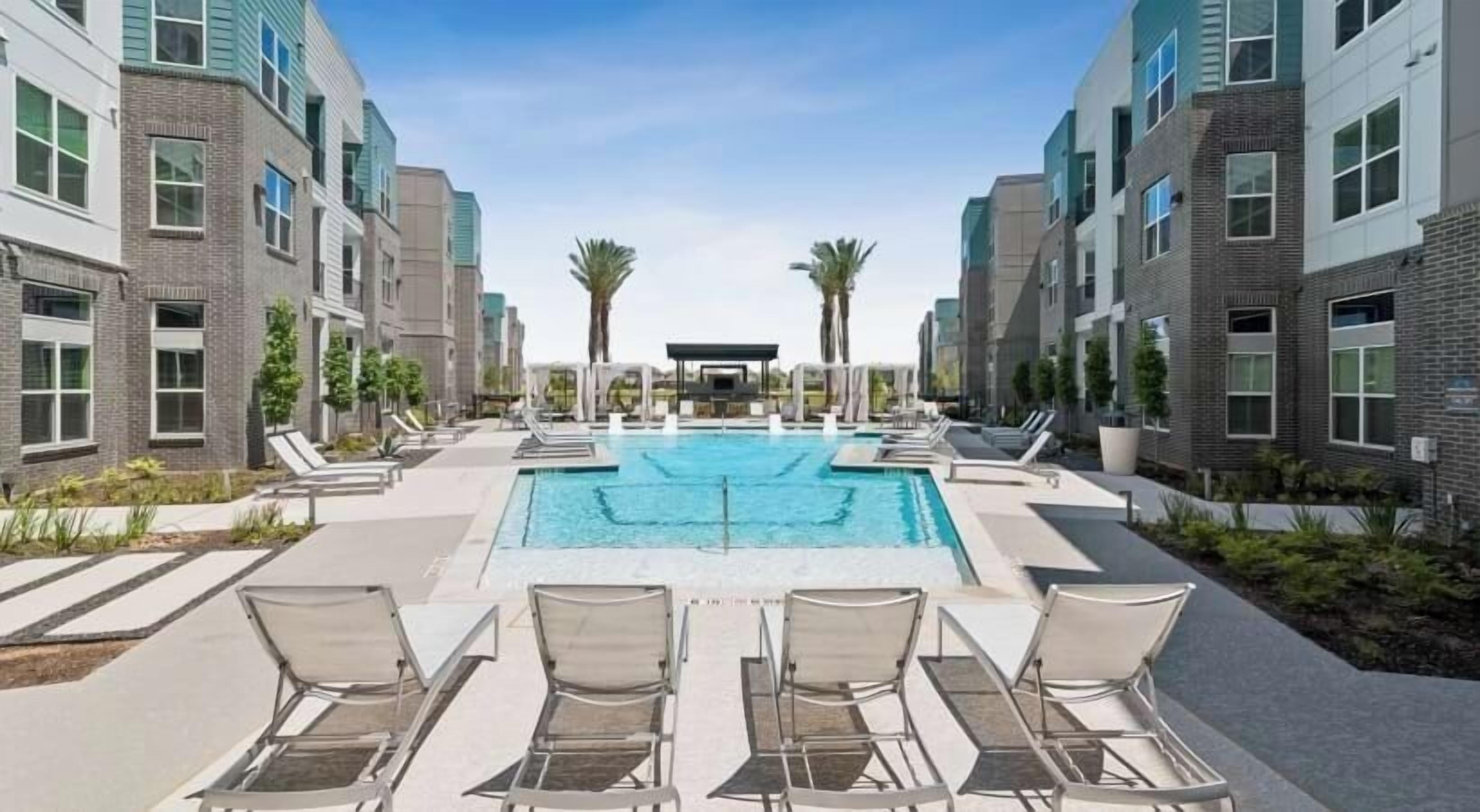A pool area with lounge chairs and a clear blue pool, surrounded by modern buildings.