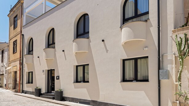Un edificio de varios pisos con fachada plana, ventanas arqueadas y un balcón en el piso superior.