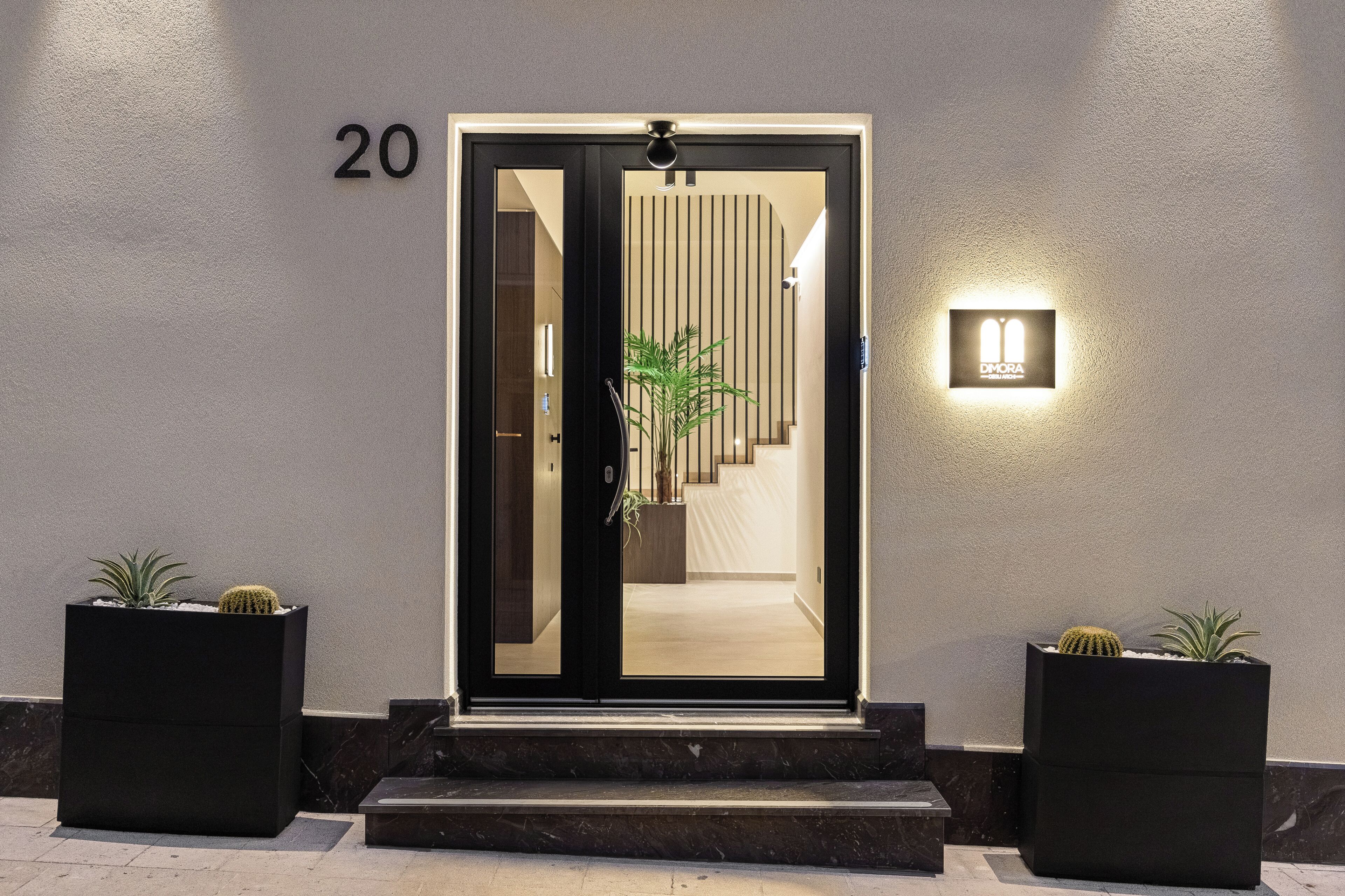 Una entrada moderna con puerta de vidrio, el número 20 en la pared y dos macetas a cada lado.