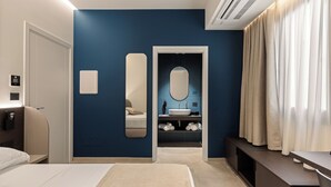 Una habitación de hotel moderna con una cama grande, una mesita de noche, un baño con lavamanos y espejo, y un vestidor.