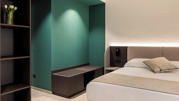 Quarto de hotel moderno com uma cama, mesa de cabeceira e um banco embutido.