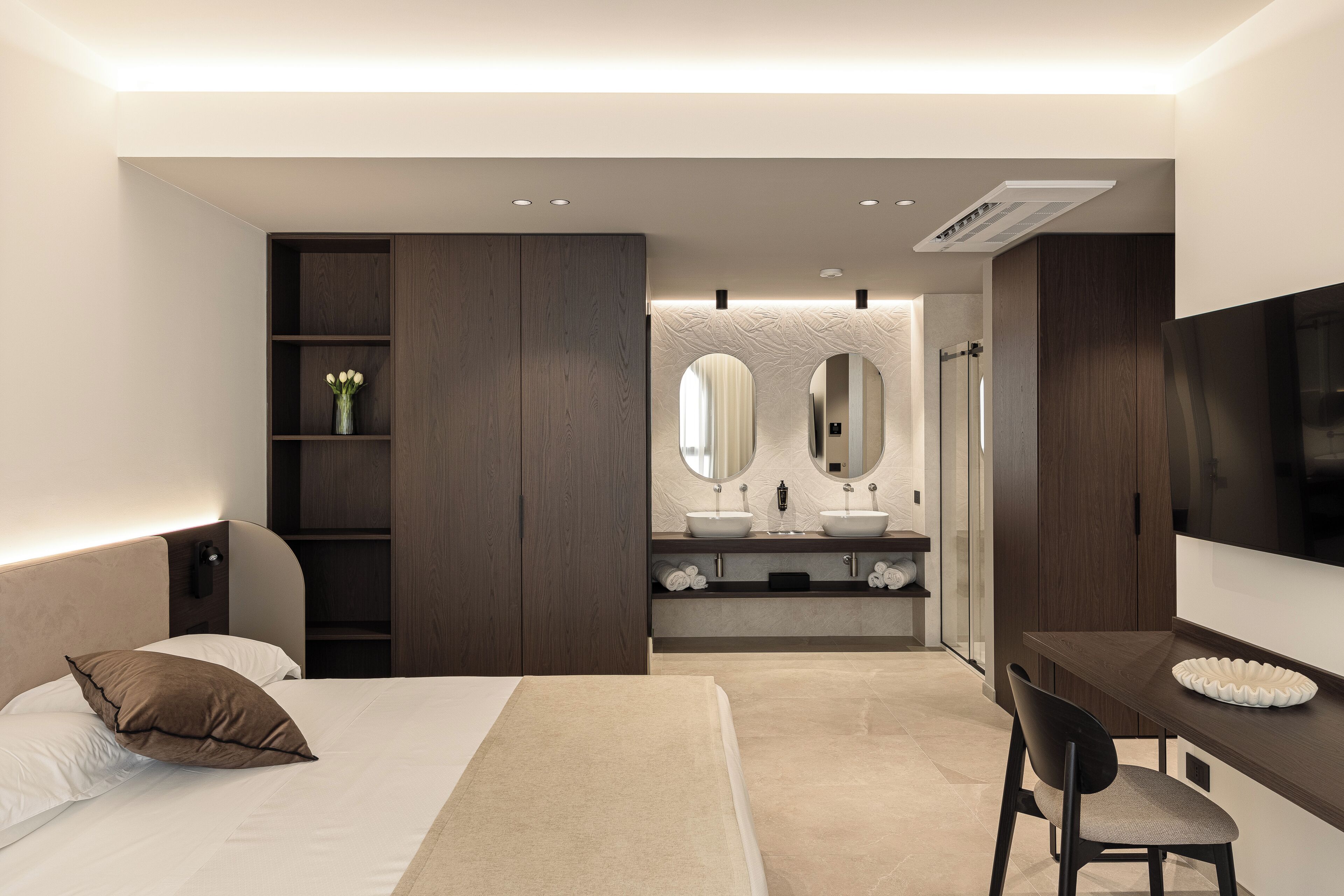 Ein modernes Schlafzimmer mit einem Bett, einem Schreibtisch und einem Badezimmer mit Waschtisch und Spiegeln.