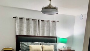 Un dormitorio con cama, mesita de noche, lámpara, ventilador de techo y cortinas estampadas.