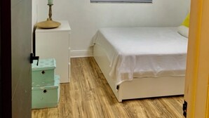 Un dormitorio con cama, ventana con persianas, ventilador de techo y un pequeño escritorio con lámpara.