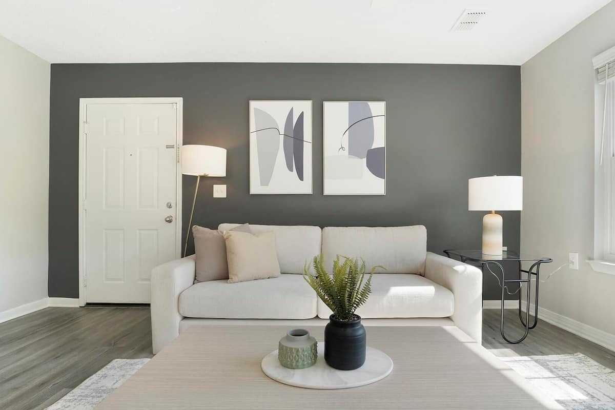 A modern living room with a gray accent wall, a white door, a sofa, two floor lamps, and a potted plant.