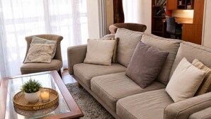 Ein Wohnzimmer mit einer Couch, einem Sessel und einem Glastisch mit Kerze und Pflanze.