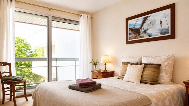 Ein Schlafzimmer mit einem Bett, einem Sessel, einem Nachttisch, einer Lampe und einem Bild an der Wand.