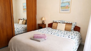 Ein Doppelbett mit floralem Überwurf, ein Holzschrank, ein Nachttisch mit Lampe und ein Poster mit einem Boot an der Wand.