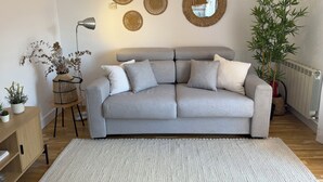 A living room with a grey sofa, a small side table with a plant, a floor lamp, and a large mirror on the wall. - Hórreo Apartment in downtown Cangas with a terrace and mountain views. (Cangas de Onís)