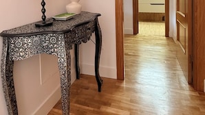 A hallway with a wooden floor, a console table with a lamp, a mirror, and a vase with dried flowers. - Hórreo Apartment in downtown Cangas with a terrace and mountain views. (Cangas de Onís)