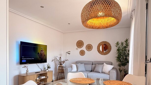 A modern living room with a glass dining table, white chairs, a grey sofa, and a television mounted on the wall. - Hórreo Apartment in downtown Cangas with a terrace and mountain views. (Cangas de Onís)