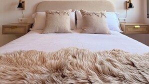 A bedroom with a large bed, two bedside tables, a ceiling light, and a fluffy rug. - Hórreo Apartment in downtown Cangas with a terrace and mountain views. (Cangas de Onís)