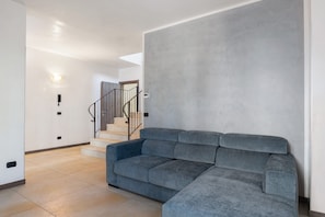 Ein modernes Wohnzimmer mit einem grauen Modulsystem, einer Treppe und einer hellen Wand.