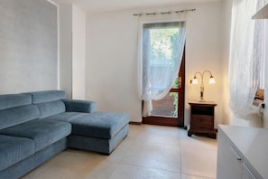 Ein Zimmer mit einer grauen Couch, einem kleinen Nachttisch mit Lampe und einem weißen Schrank.