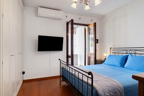 Ein Schlafzimmer mit einem Bett, einem an der Wand montierten Fernseher, einem Holzboden und einer Tür zu einem anderen Raum.