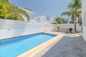 Una piscina con escalones que llevan al borde, rodeada por un muro blanco y palmeras.