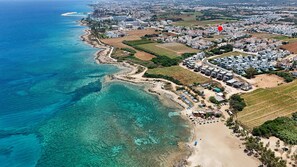 An aerial view of a coastal town with clear blue waters, a sandy beach, and residential buildings.