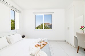 A hotel room with a bed, a window with a view, a wardrobe, and a small table with a tray.