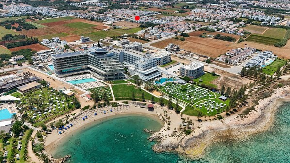 An aerial view of a coastal hotel with multiple buildings, a beach, and clear blue waters.