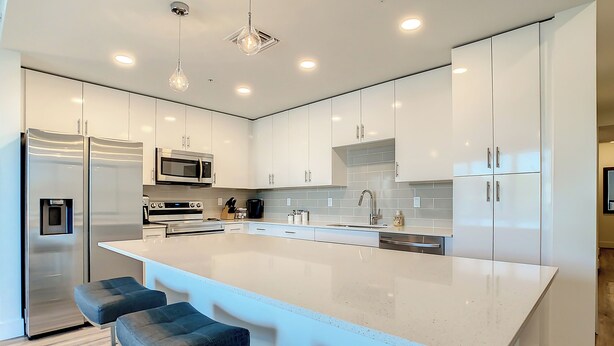 Una cocina moderna con armarios blancos, electrodomésticos de acero inoxidable y una isla central con taburetes de bar.