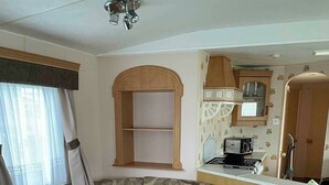 Een compacte leefruimte met een bank, een kitchenette en een raam met gordijnen.