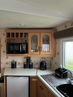 A compact kitchen with a refrigerator, microwave, cabinets, and a kettle.