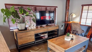 A living room with a TV, wooden furniture, a plant, and a lamp.