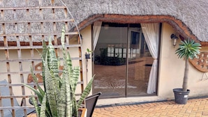 A thatched-roof building with a sliding glass door, a potted plant, and a metal chair.