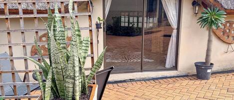 Edificio con techo de paja, puerta corredera de vidrio, planta en maceta y una silla de metal.