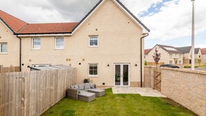A residential building with a sloped roof, a wooden fence, a grassy yard, and a patio area. - Annie Paton Road (No 123) | St Andrews (St Andrews)