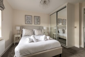 A bedroom with a large bed, two bedside tables with lamps, a mirror, and artwork on the wall. - Annie Paton Road (No 123) | St Andrews (St Andrews)