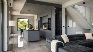 Eine moderne Küche mit einer zentralen Kochinsel, einem Essbereich mit einem Stuhl, einer Couch und einer Treppe.