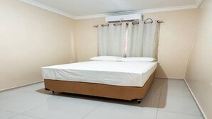 Una habitación pequeña y limpia con una cama individual, una ventana con cortinas y piso de baldosas.