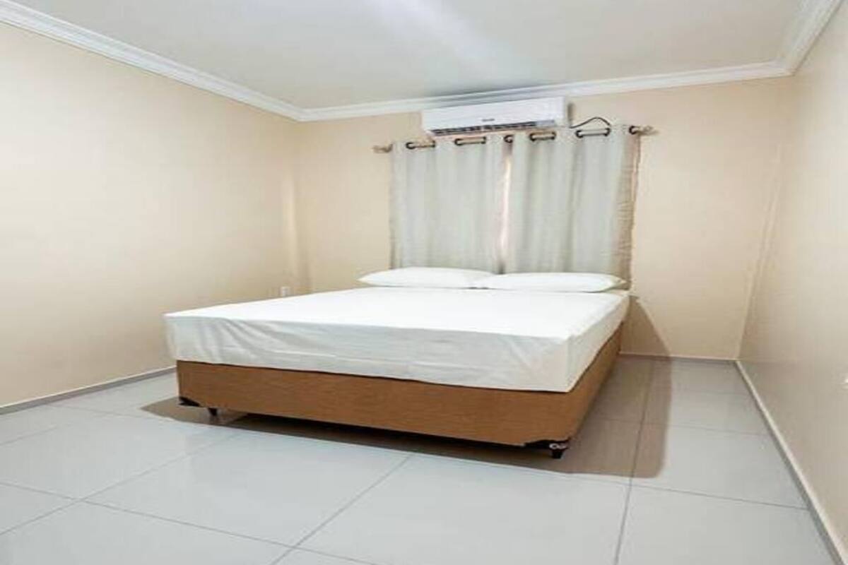A small, clean room with a single bed, a window with curtains, and a tiled floor.