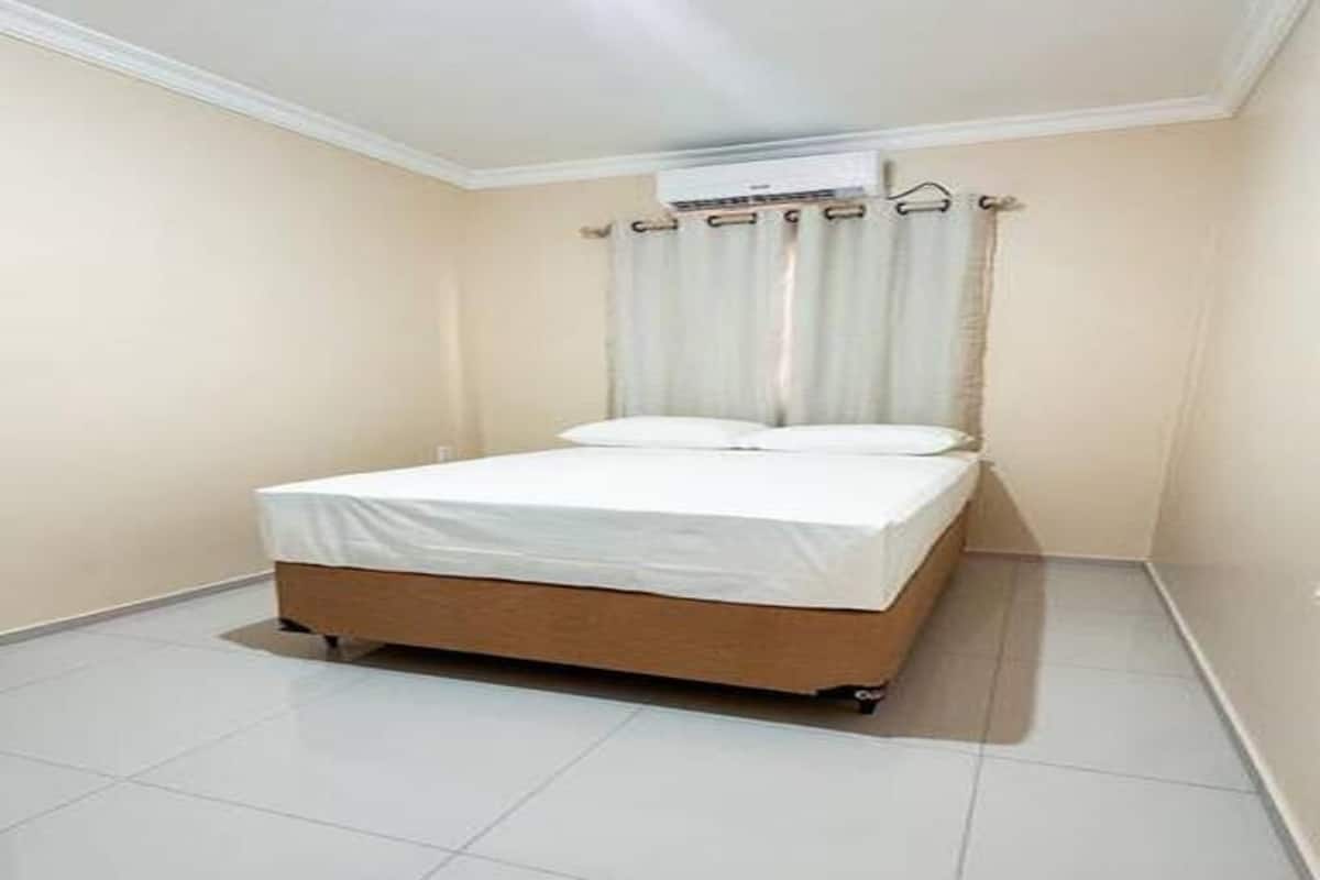 A small, clean room with a single bed, a window with curtains, and a tiled floor.
