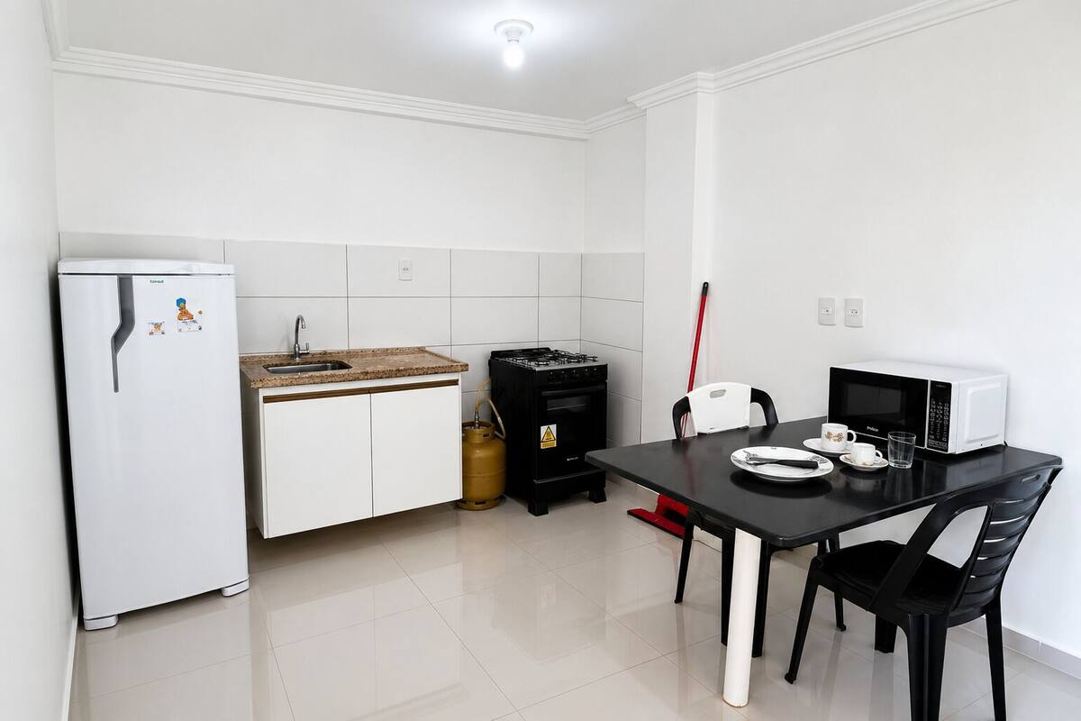 A compact kitchen with a refrigerator, sink, stove, microwave, and dining table with chairs.
