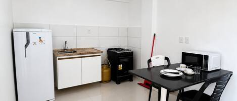 A compact kitchen with a refrigerator, sink, stove, microwave, and dining table with chairs.