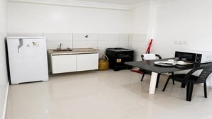 Una cocina compacta con muebles blancos, un refrigerador, una estufa a gas y una mesa con sillas.