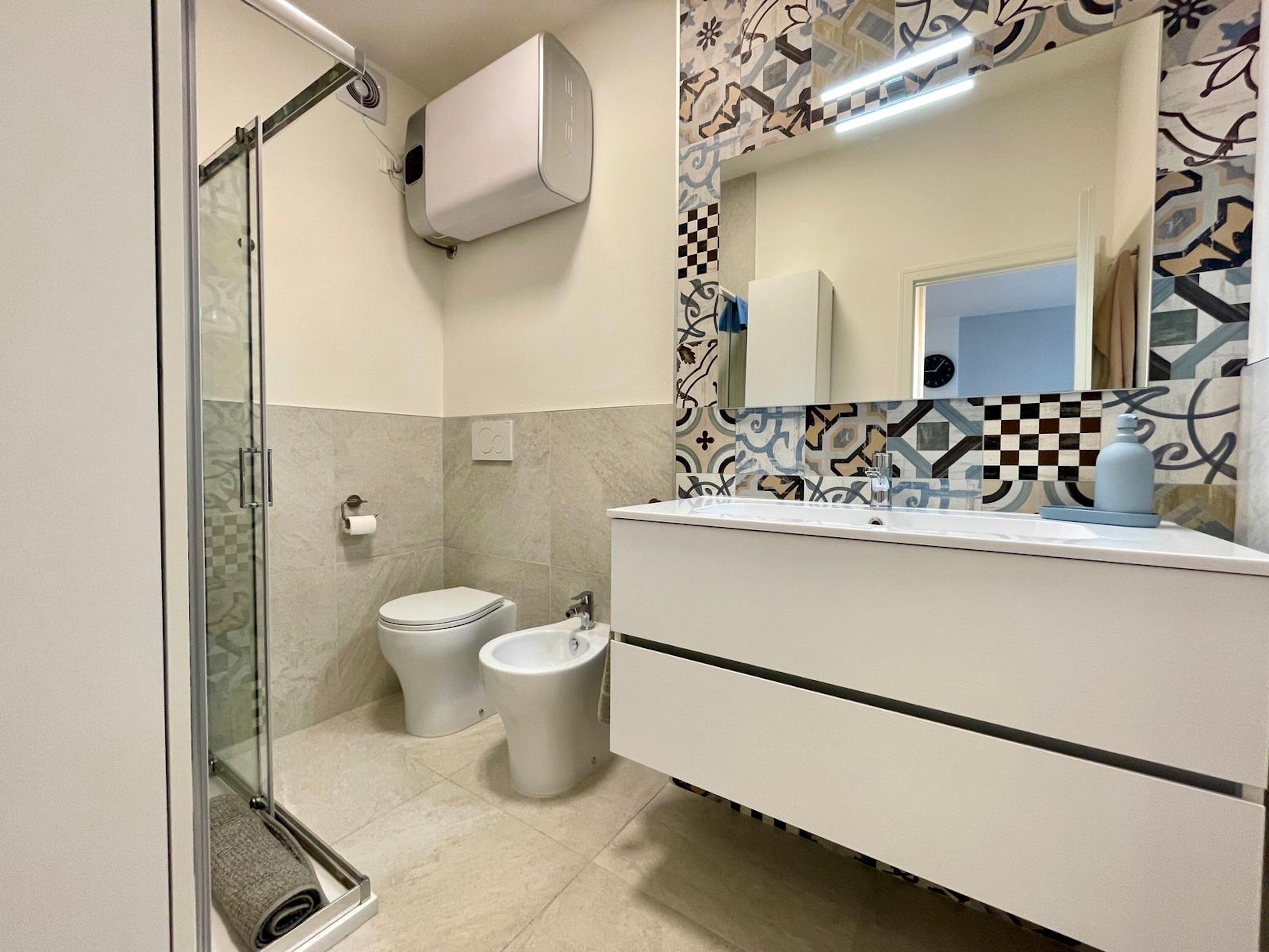 Une salle de bain moderne avec une douche à parois de verre, des toilettes, un bidet et un meuble-lavabo avec un miroir.