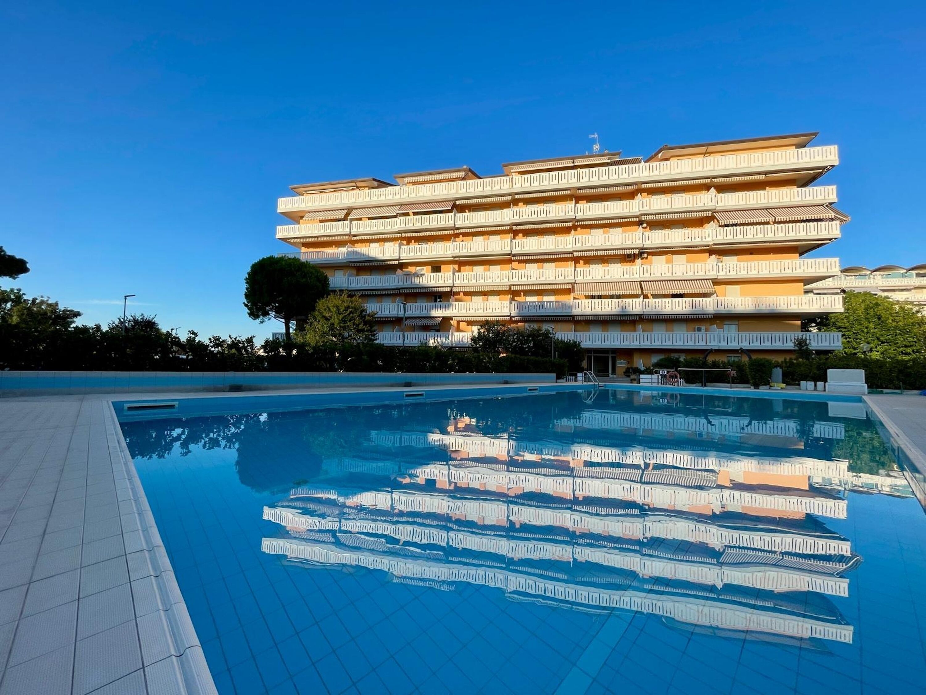 Et hotel med flere etager, altaner, en swimmingpool og en klar blå himmel.
