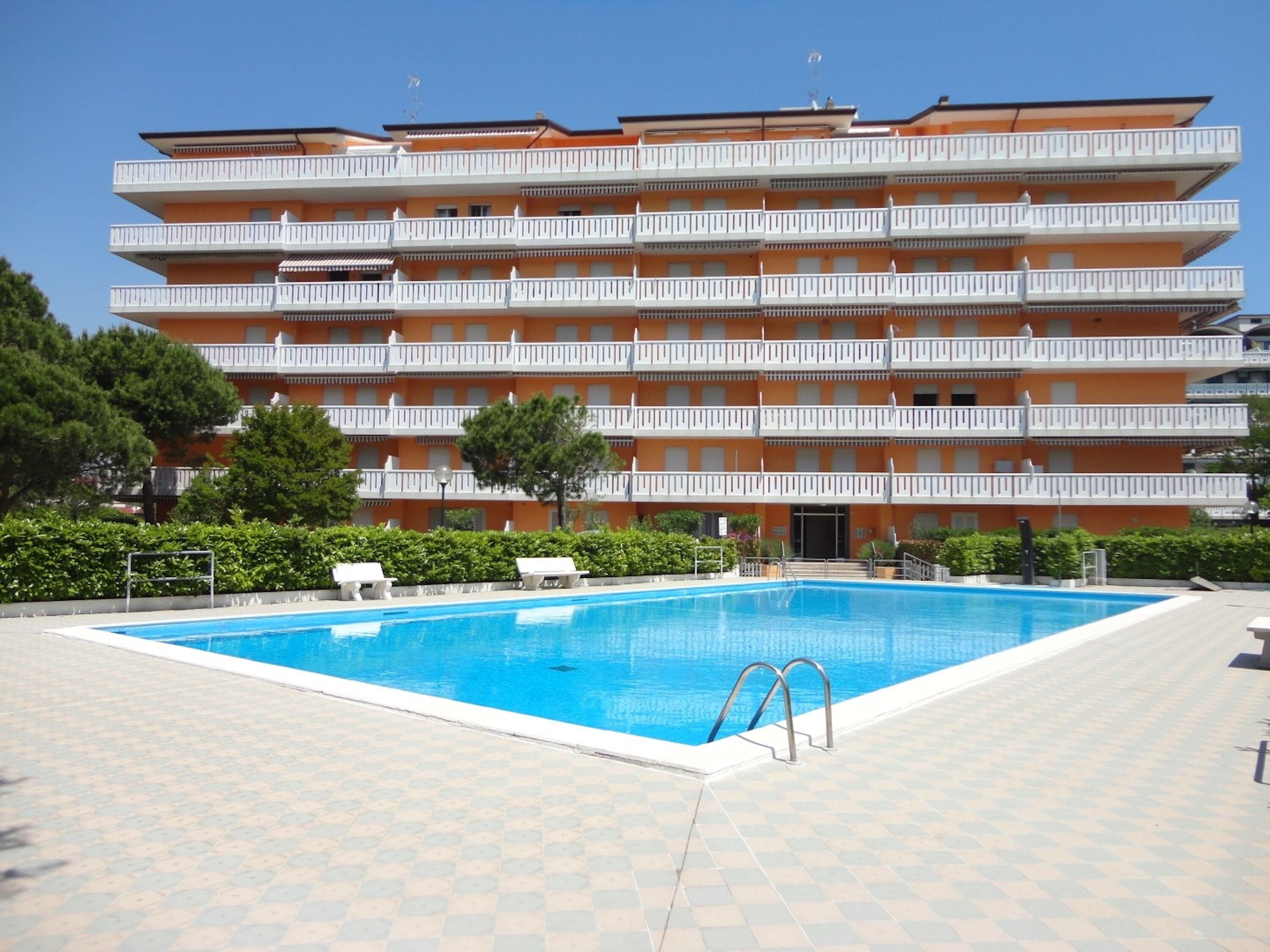 A multi-story hotel with a swimming pool, outdoor seating, and a well-maintained garden.