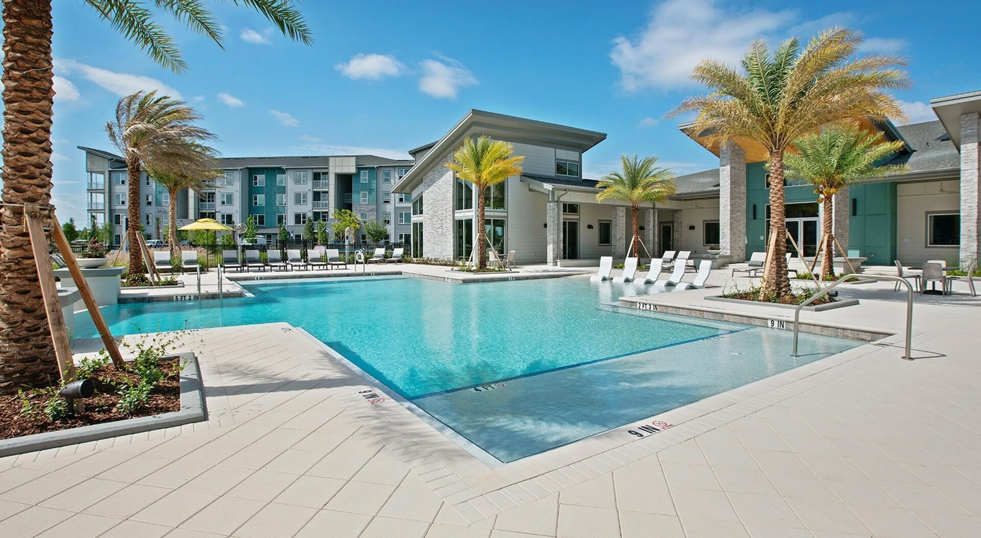 A pool area with lounge chairs, palm trees, and a modern building in the background.