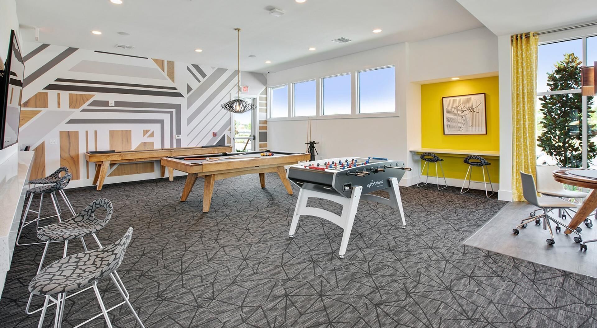 A modern indoor space with a pool table, foosball table, and bar stools.