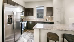 Une cuisine moderne dotée d’appareils électroménagers en acier inoxydable, de plans de travail en granit et d’armoires en bois foncé.