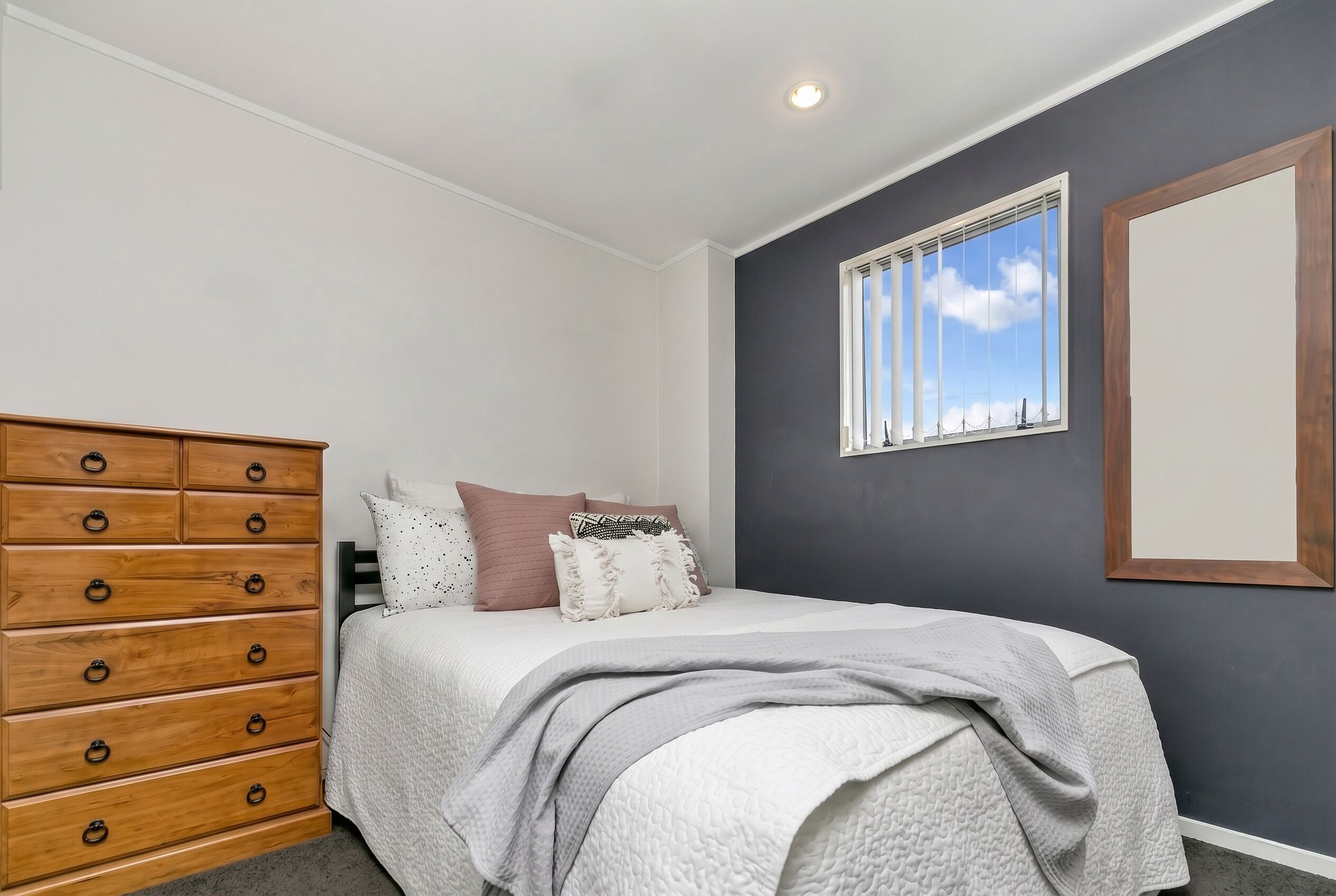 Une chambre à coucher avec un lit, une commode, une fenêtre et un tableau encadré au mur.