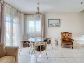 A spacious living room with a round glass table, gold chairs, a brown velvet armchair, a chandelier, and a painting on the wall. - Ambela House too, in the Heart of Kefalos, Kos (Kefalos)