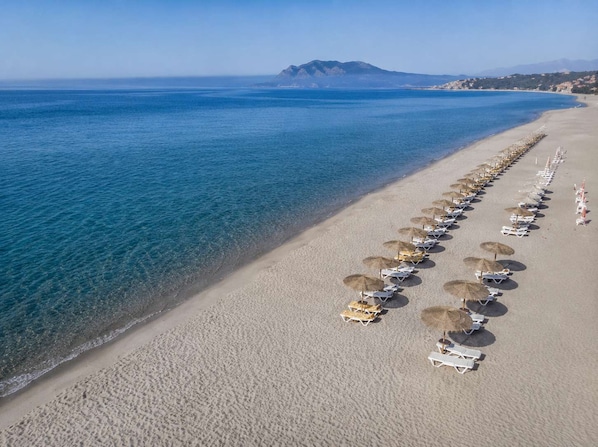 An aerial view of a beach with rows of sun loungers and umbrellas, a clear blue sea, and a distant mountain. - Ambela House too, in the Heart of Kefalos, Kos (Kefalos)