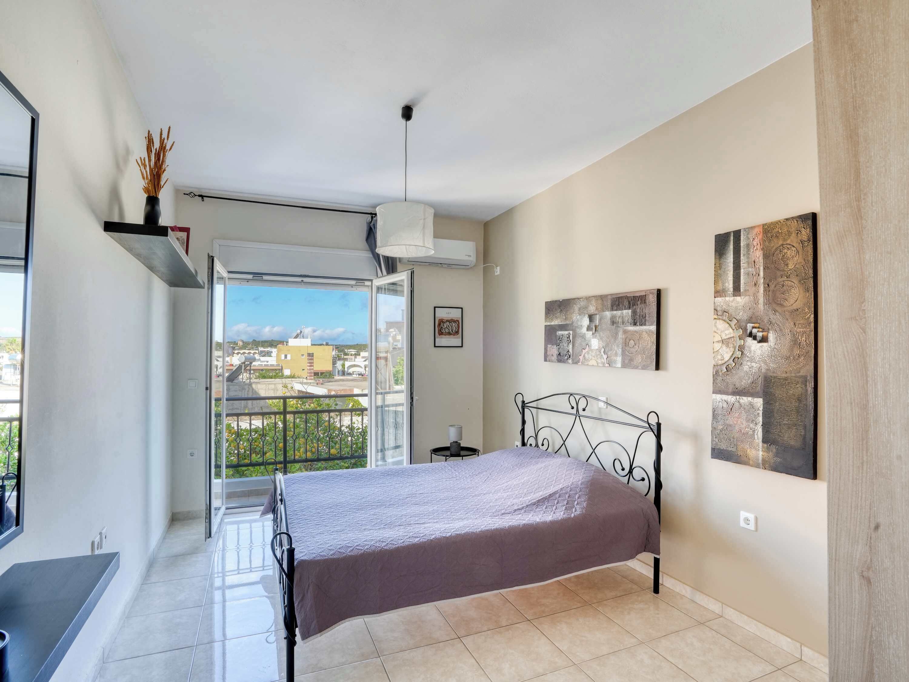 Un dormitorio con cama, balcón y vista a la ciudad, además de un cuadro en la pared.