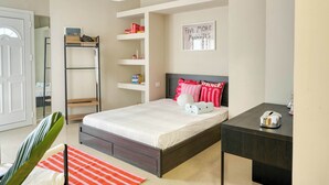 Quarto com cama, mesa de cabeceira, prateleiras e porta.