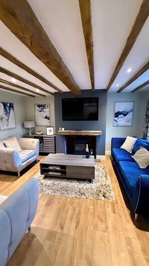 Ein Wohnzimmer mit Kamin, einem an der Wand befestigten Fernseher und einem blauen Sofa.